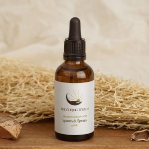 The Curing Touch Spasm & Sprain Oil on a wooden board with pampas grass in the background